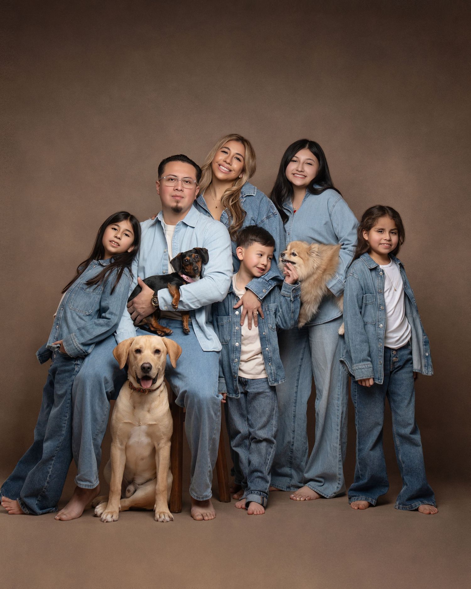 Family wearing matching denim outfits poses together with their golden labrador dog in studio portraits.