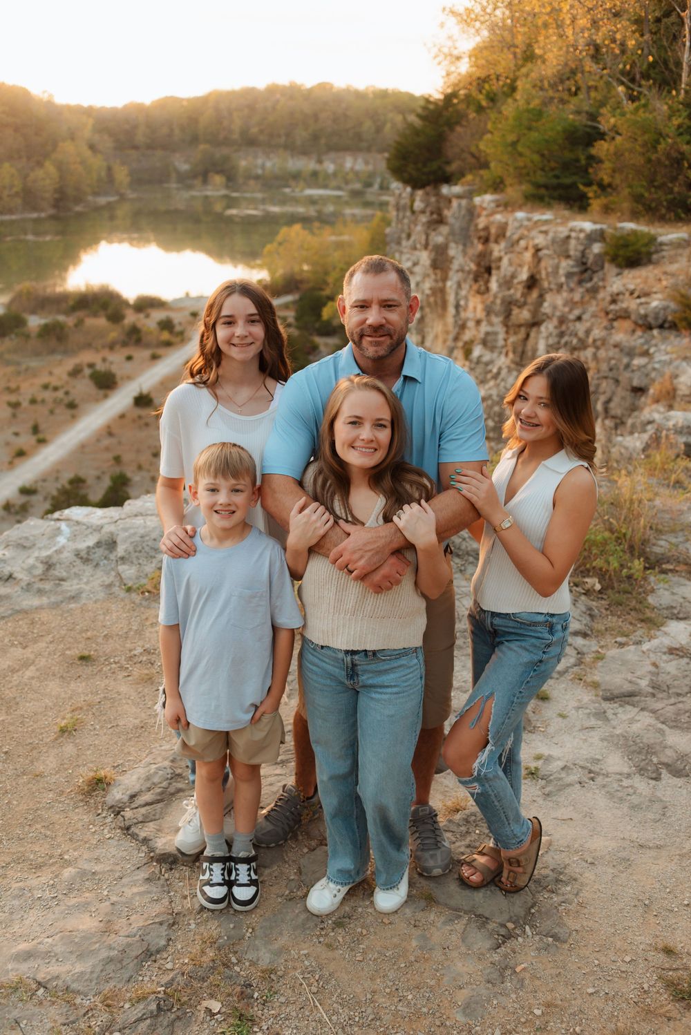 Family poses together at sunset on rocky cliff overlooking scenic lake.