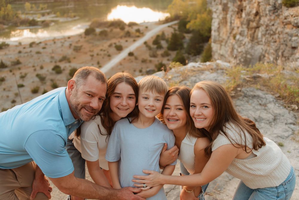 Group huddled close together laughing on rocky overlook at golden hour.