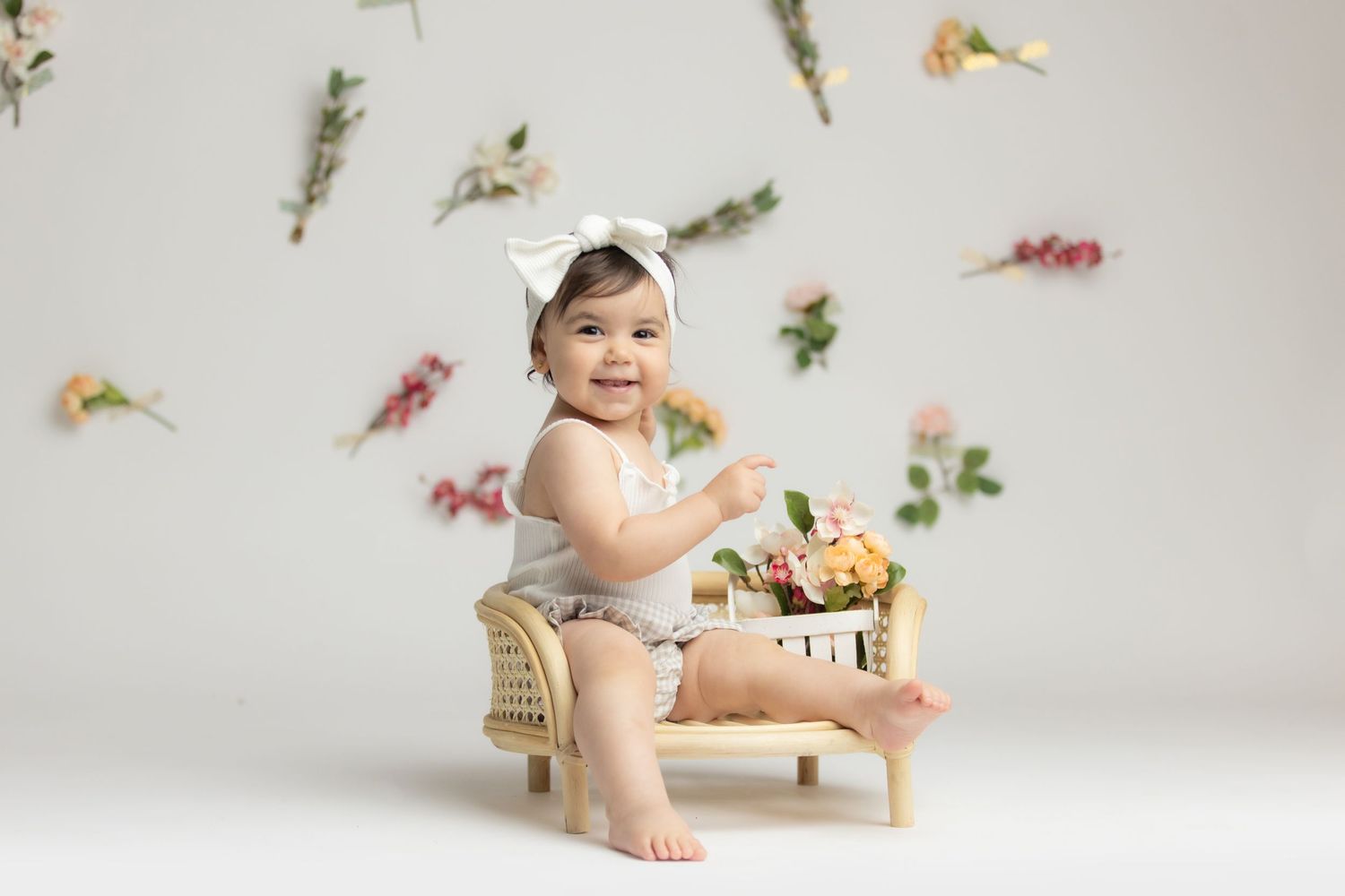 Small child sits on wooden chair with floral backdrop in professional studio photography setting.