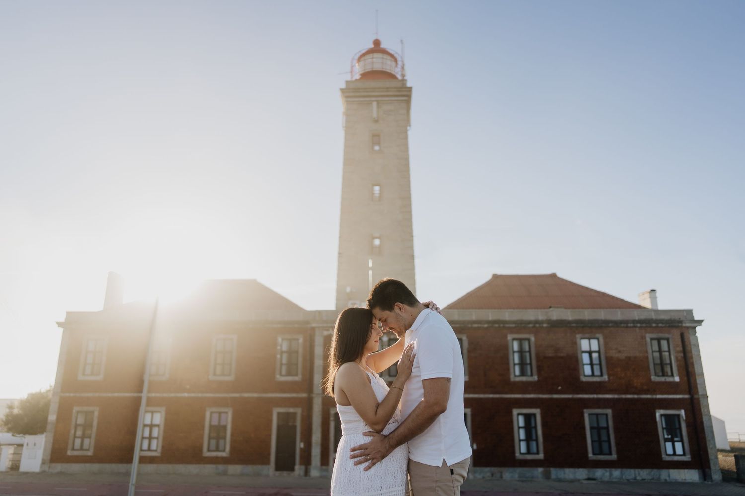 Lighthouse building silhouetted against bright sunlight with lens flare creating a dramatic backlit effect.