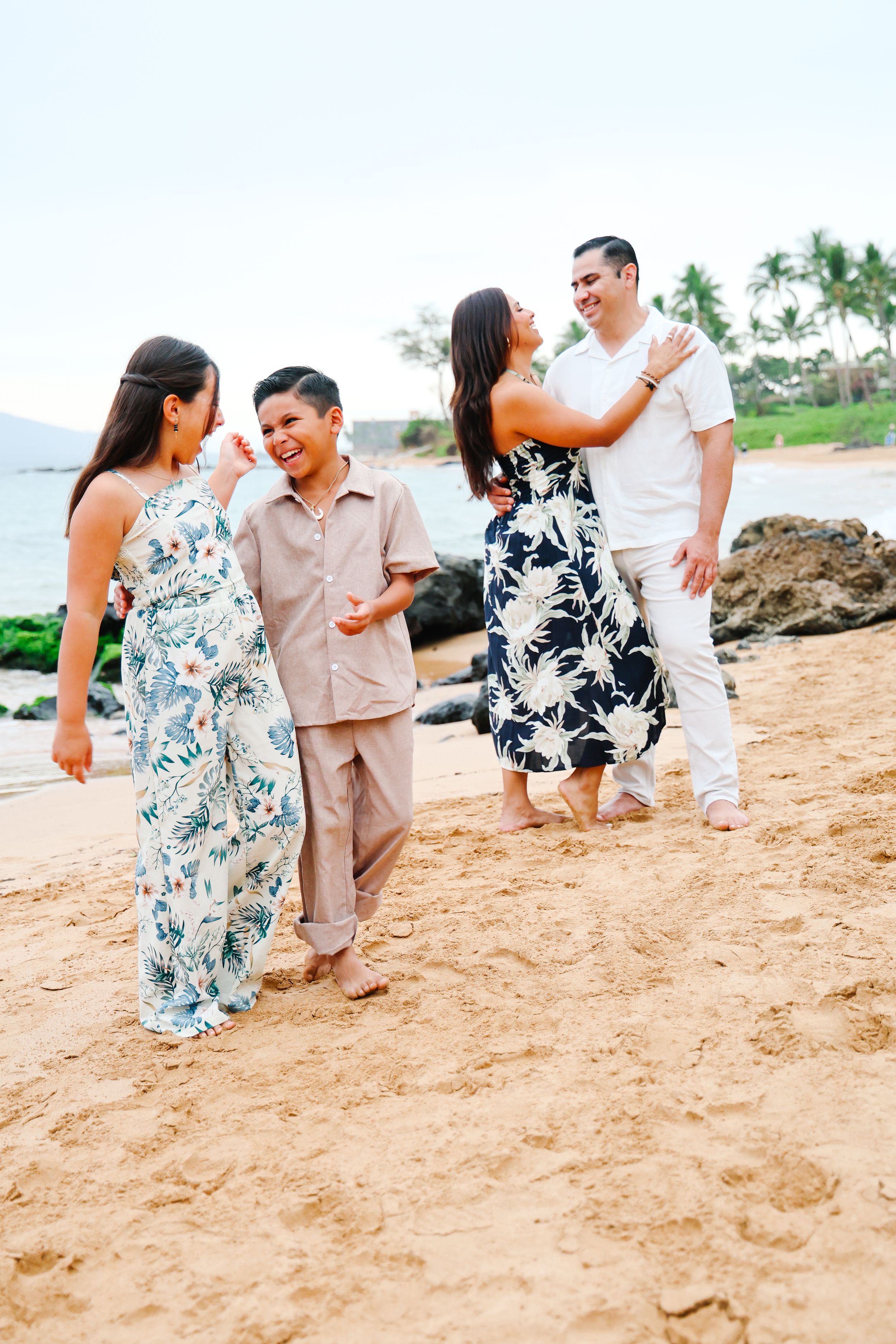 Two couples in coordinating floral outfits share joyful moments together on a tropical beach with palm trees.