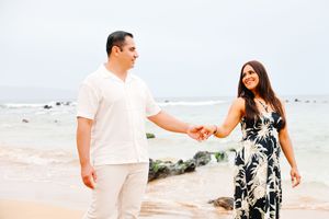 A couple dances together on a scenic beach with waves and rocks visible in the distance.