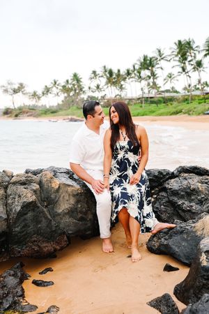 Couple sitting together on volcanic rocks at a tropical beach with palm trees in the background.