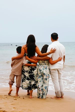 Family members in coordinated outfits sitting together on a sandy beach watching the ocean waves.