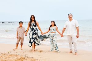 Family members in light colored clothing walking together and holding hands along a sunny tropical beach.