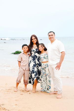 Family group posing on a tropical beach wearing coordinated white and floral outfits.