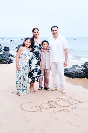 Family enjoying a beach photoshoot near black volcanic rocks with ocean waves in the background.