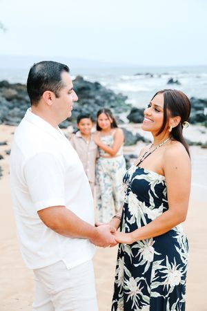 A couple shares a tender moment on the beach while others watch in the background.