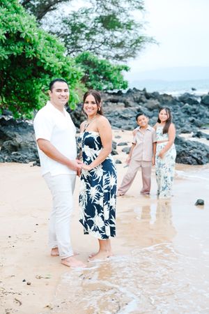 People in coordinated white and navy outfits walk along a scenic beach with volcanic rocks and waves.