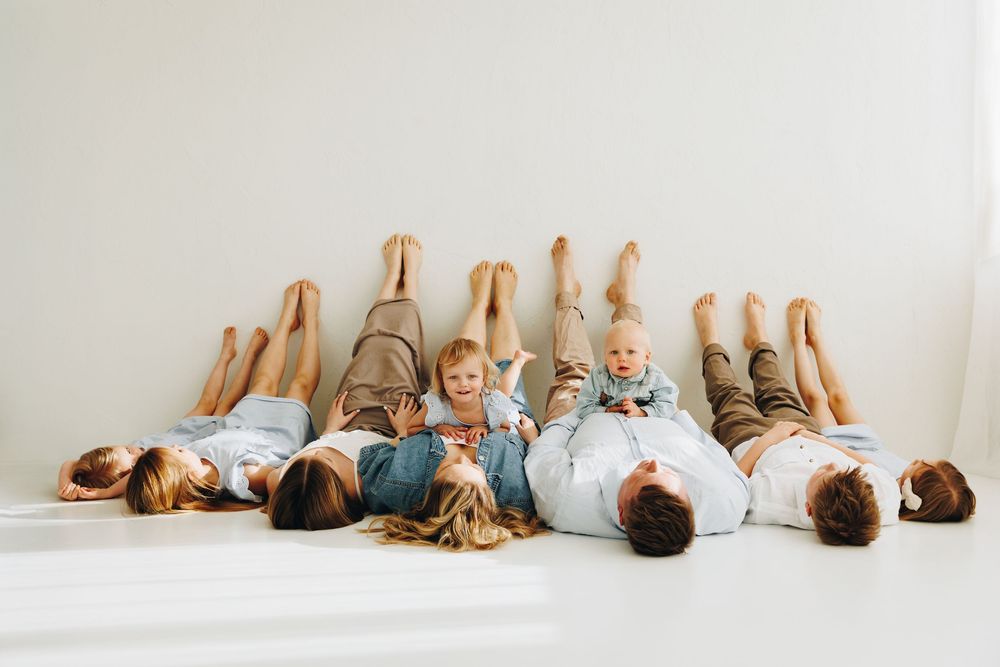 Family with children lying on floor with legs up against white wall in a fun and playful posed photo.