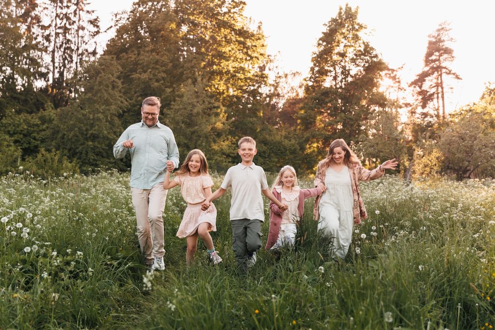 Happy family with three children running through a sunny wildflower meadow with golden trees in the background.