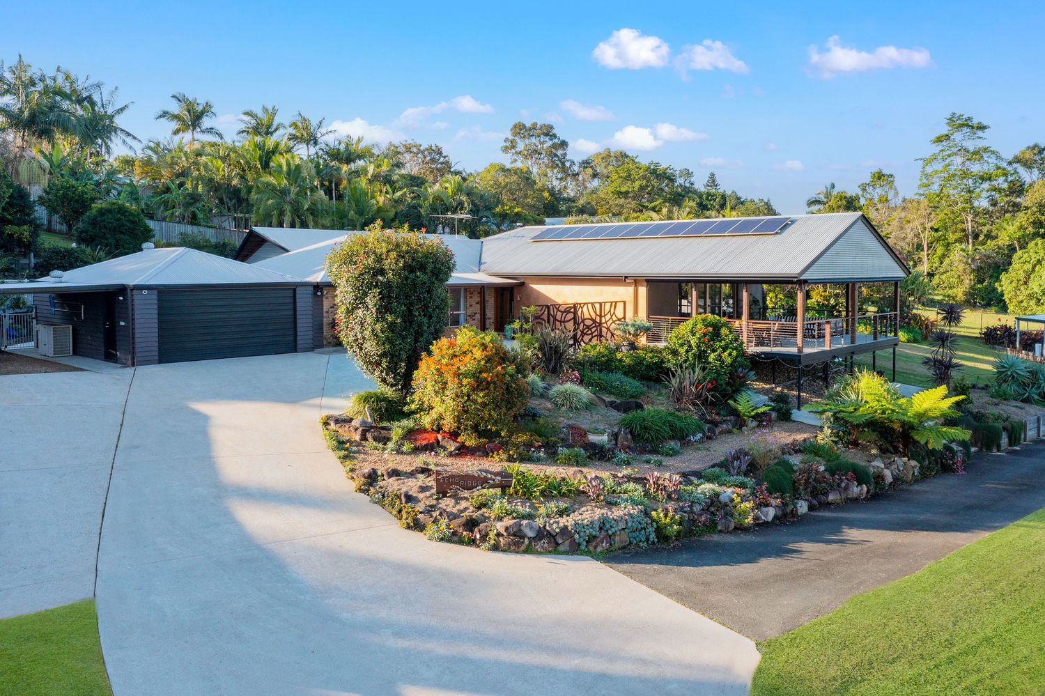 Aerial view of a spacious Australian home with curved driveway, lush tropical gardens, and a covered entertaining area.