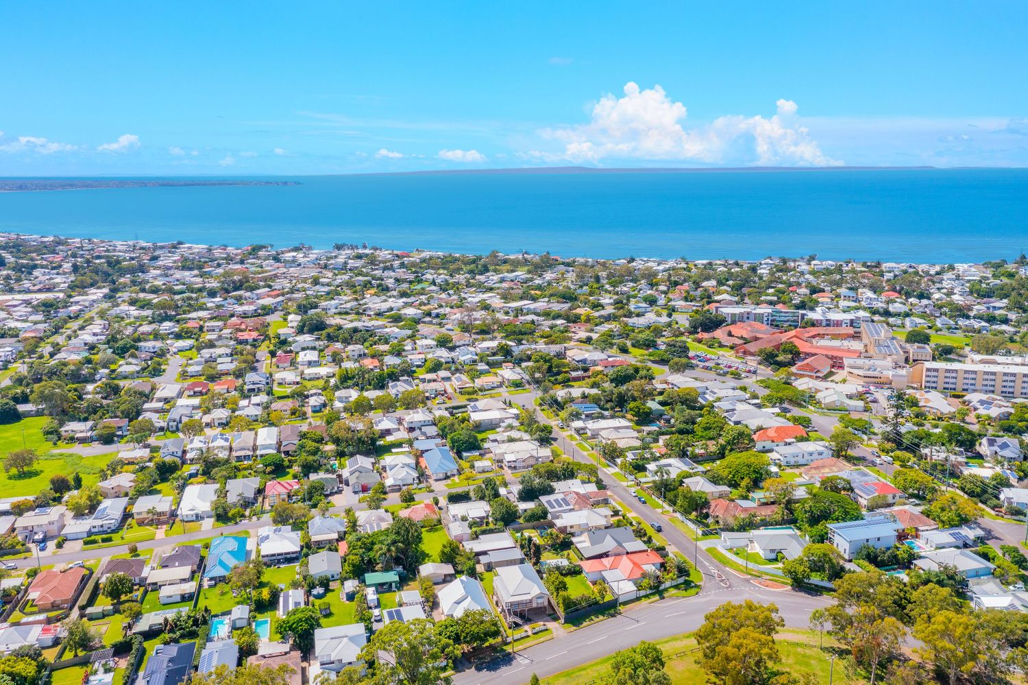 Aerial view of a coastal Australian suburb with ocean views, green parks, and residential streets near the beach.