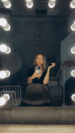 Valokuvaaja Polina Khanteeva istuu valaistun peilin edessä ja katsoo kameraan.