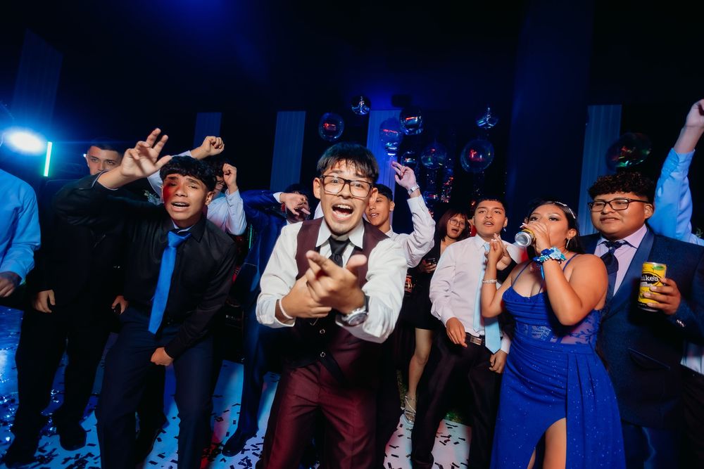 Wedding party guests dancing and celebrating on a dark dance floor illuminated by blue lighting effects.