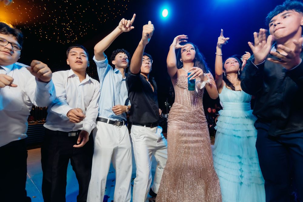 Wedding guests dance and celebrate together on a dimly lit dance floor with blue lighting in the background.