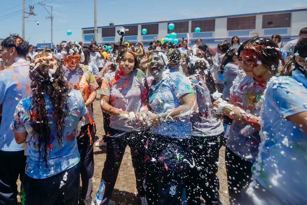 A crowd of people spraying and splashing water at each other during a festive outdoor celebration in bright sunlight.