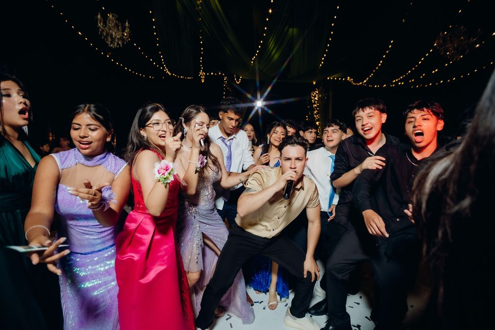 People dancing and celebrating at a dimly lit nighttime party with string lights overhead.