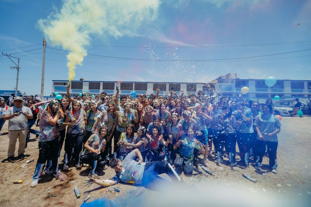 Large crowd celebrates outdoors with colorful smoke effects in front of a commercial building.