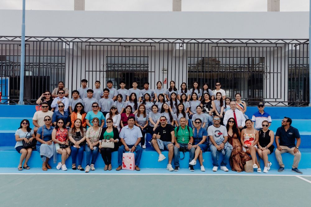 Large group of students sitting together on blue outdoor court for group photo.