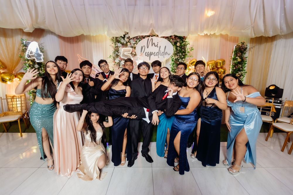 Wedding party members sit together in formal attire inside an elegant white-draped reception venue.