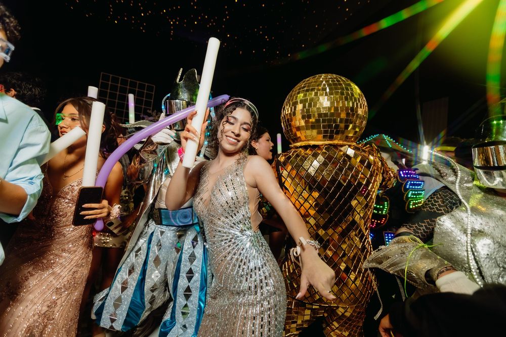 Partygoers dance and celebrate under a glittering disco ball with light-up foam sticks at a nightclub event.