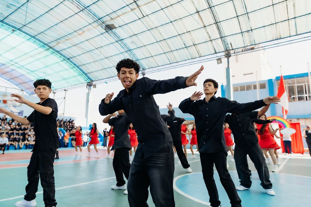 Students perform synchronized dance moves during a group performance in an indoor gymnasium.