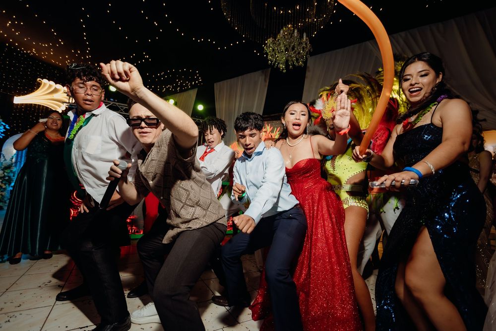 Energetic crowd dances and celebrates at a festive reception with dramatic overhead lighting.