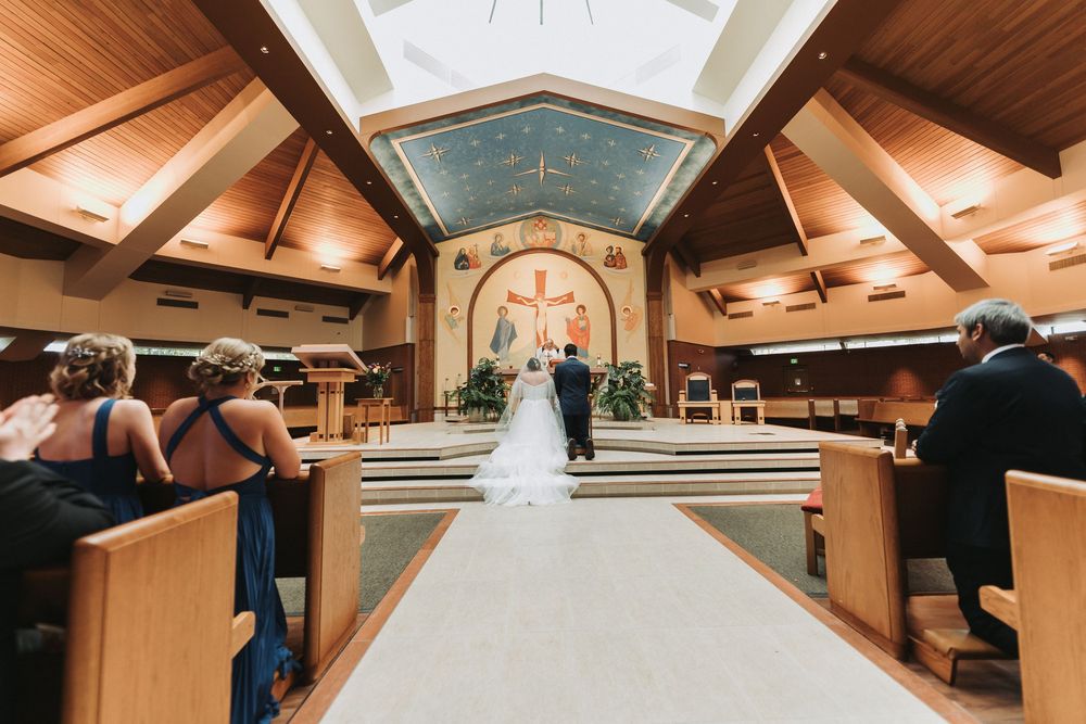 A wedding ceremony takes place in a modern church with wooden beams and a vaulted ceiling with skylight.
