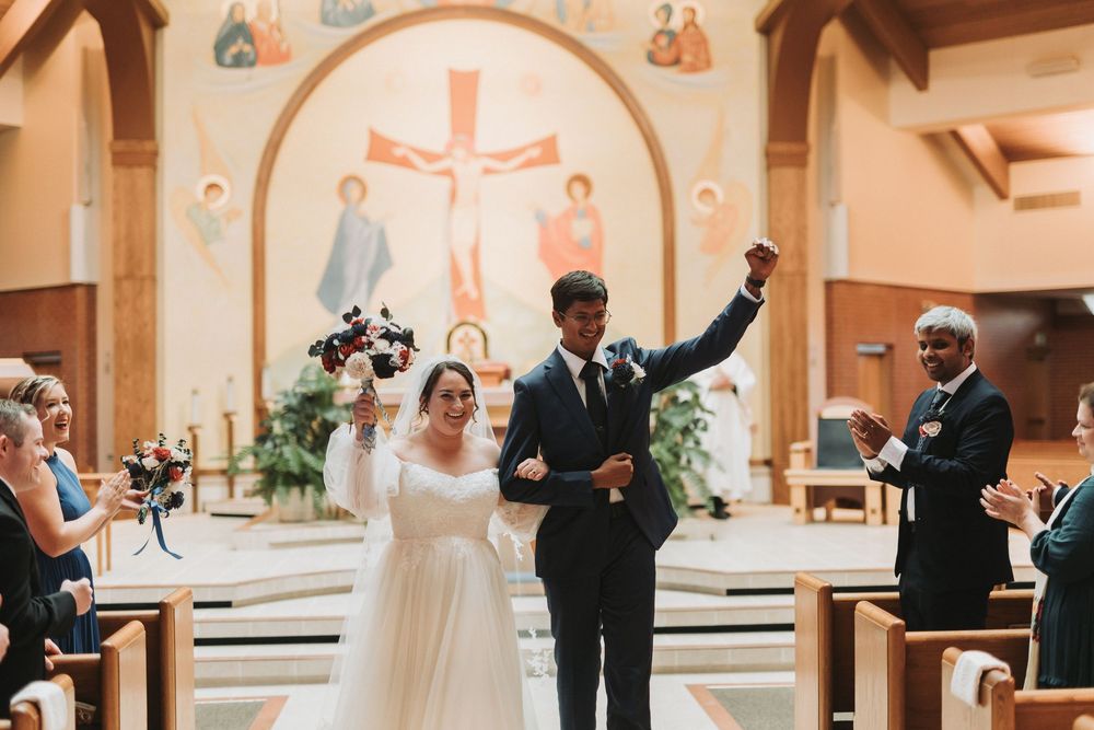 Wedding party members celebrate joyfully while walking down the aisle at a church ceremony.