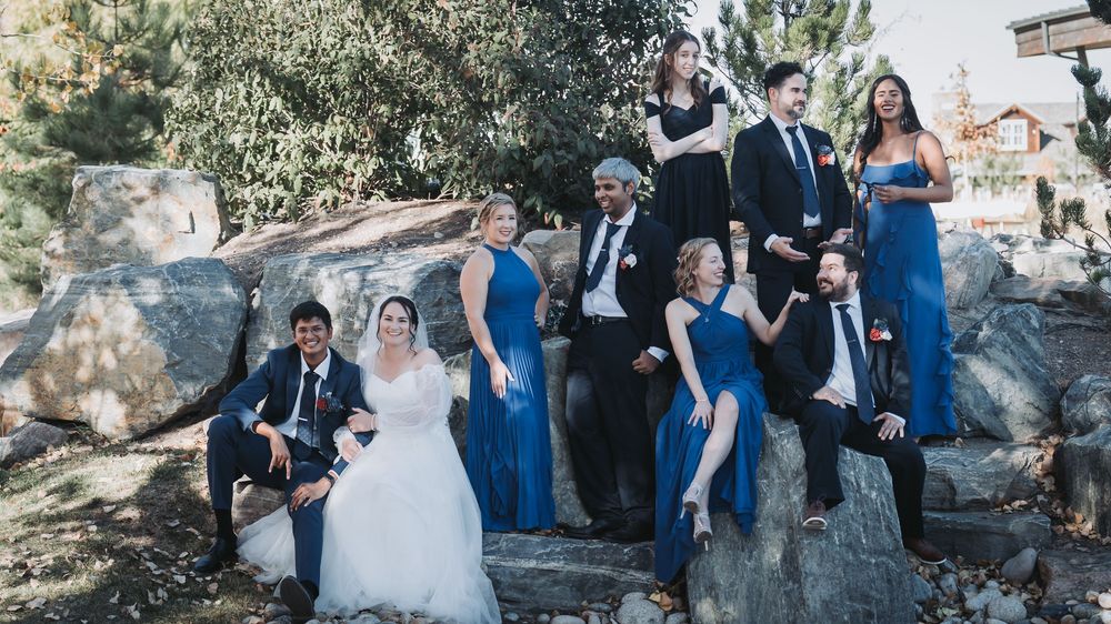 Wedding party in formal attire poses together on rocky terrain with blue and black color scheme.
