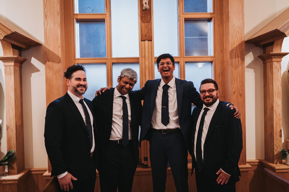 A group in formal attire poses together in a rustic wooden room with large windows.