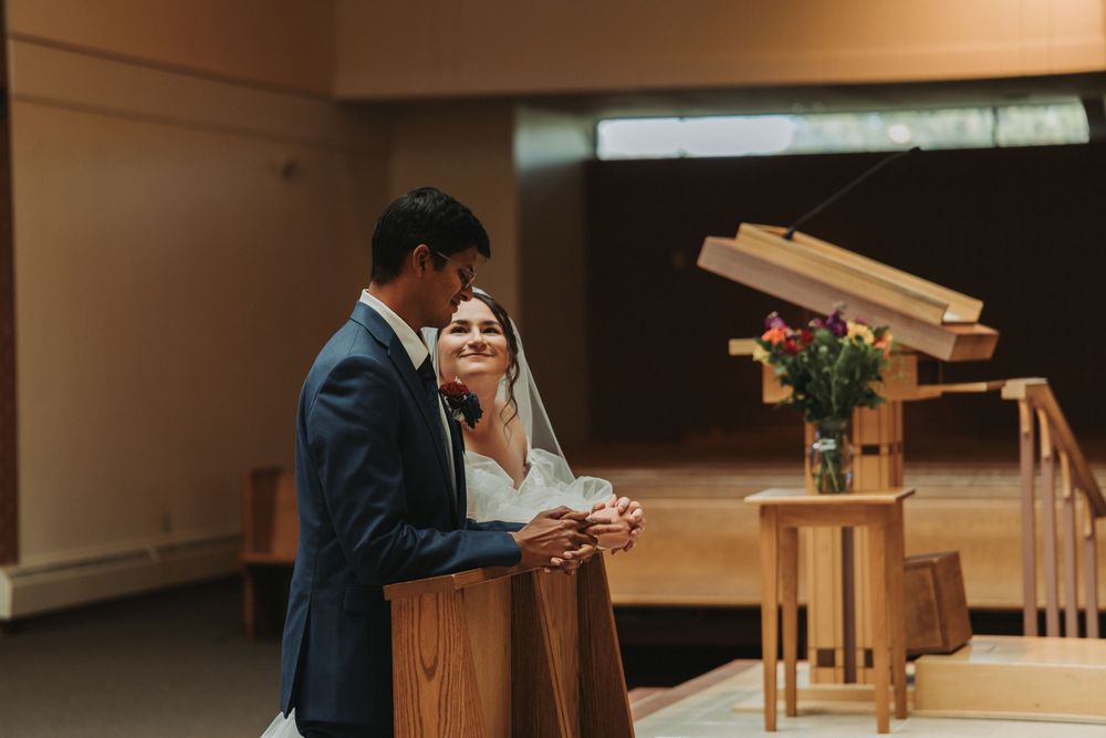 People seated in church pews during a formal ceremony with wooden architectural details.