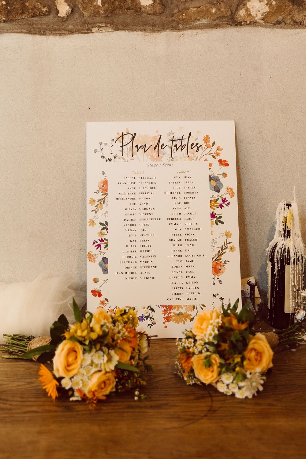 Wedding seating chart with floral decorations and yellow roses displayed on a rustic wooden table with vintage bottles.