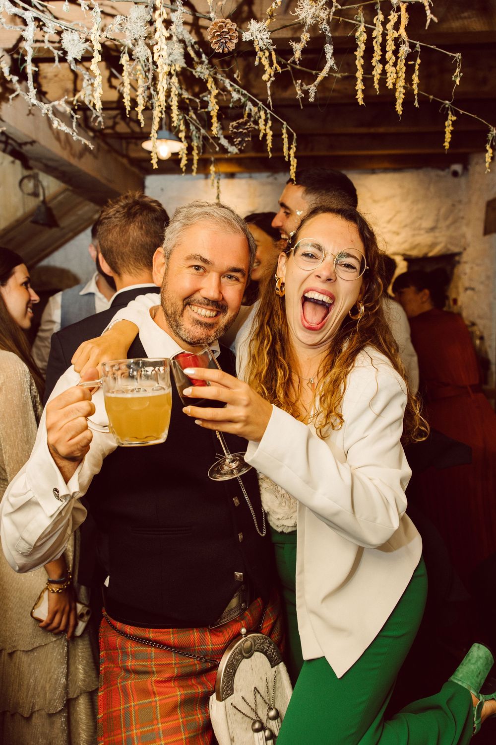 Two people laughing and enjoying beer together at a rustic pub with festive decorations overhead.
