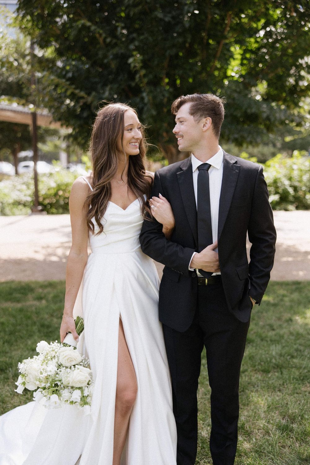 Bride in white dress and groom in black suit posing casually outdoors.