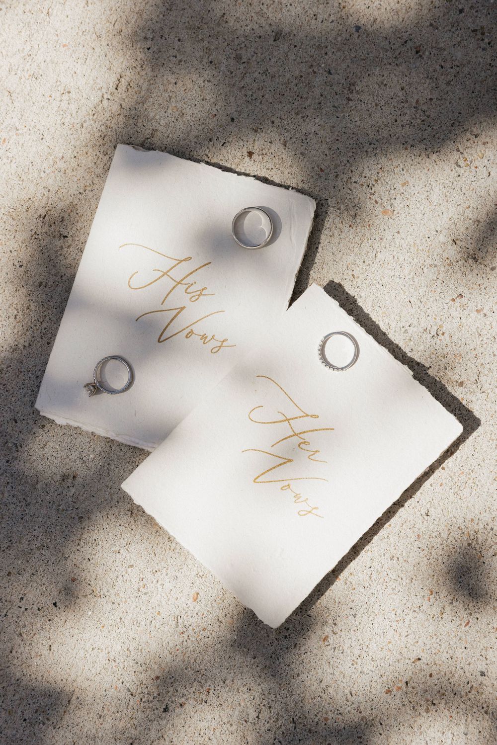 Wedding invitation cards with gold lettering laid out in sunlight and shadow.