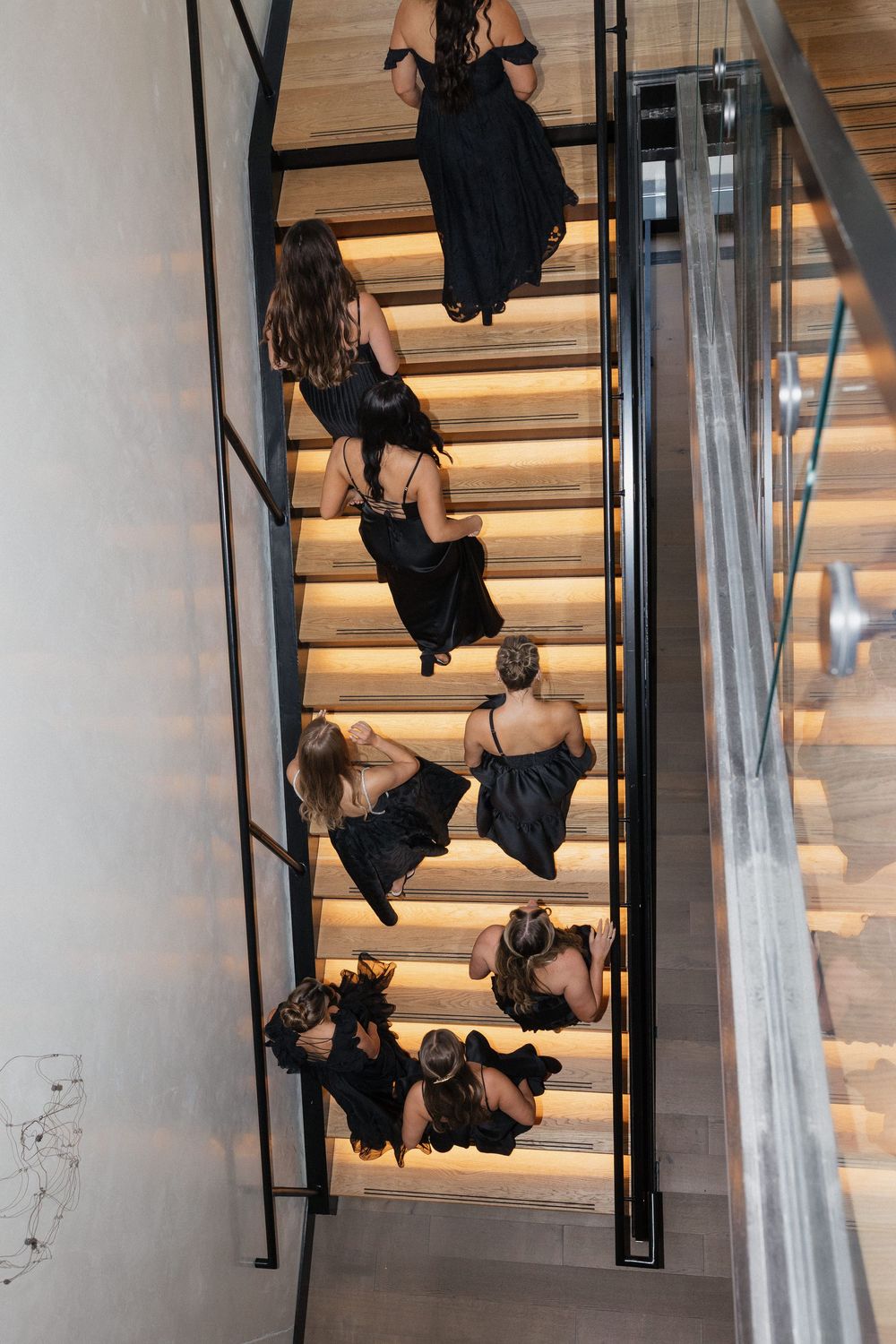 Group descending modern staircase in formal attire during wedding event.