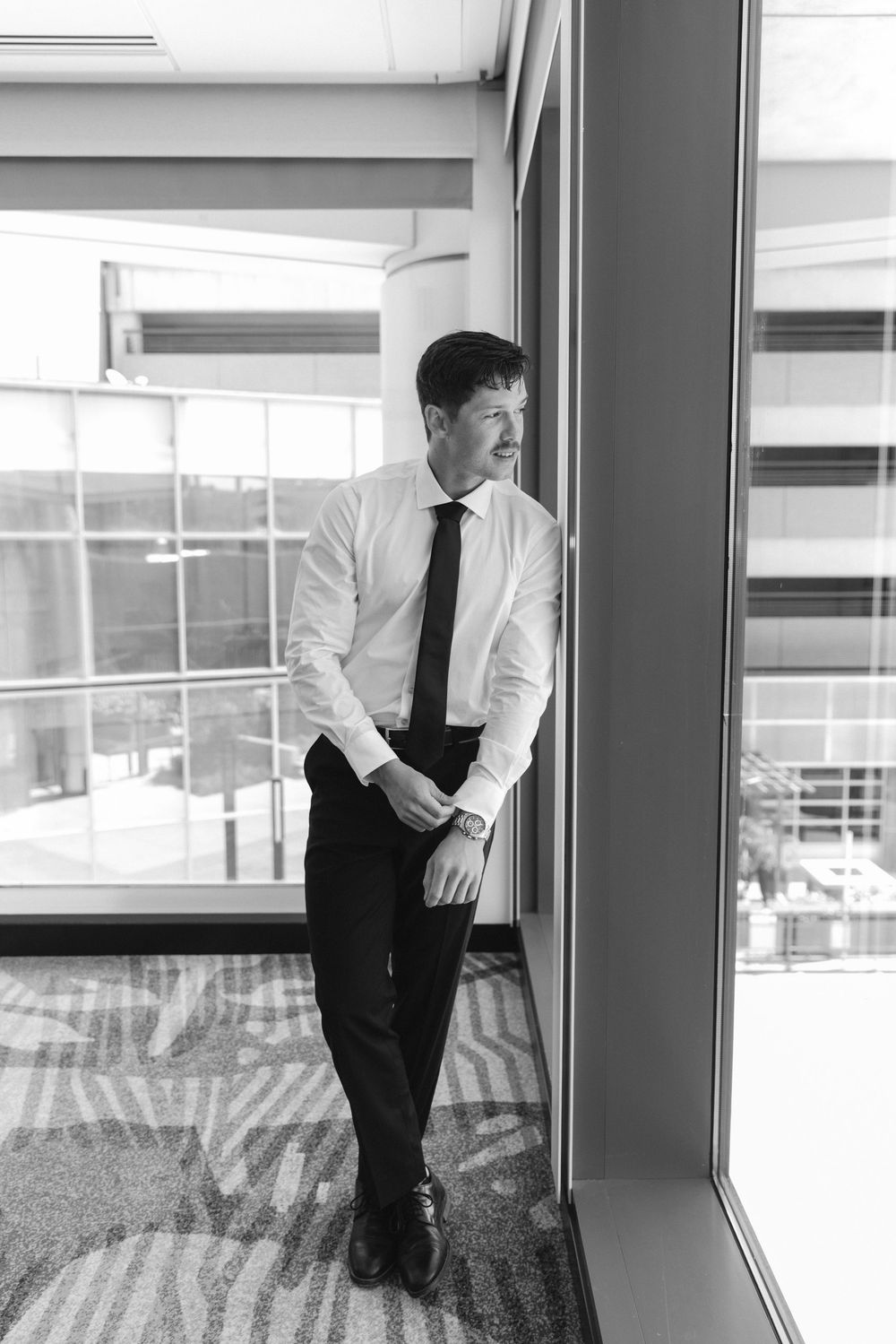 Person in formal attire looking out large windows in modern building.