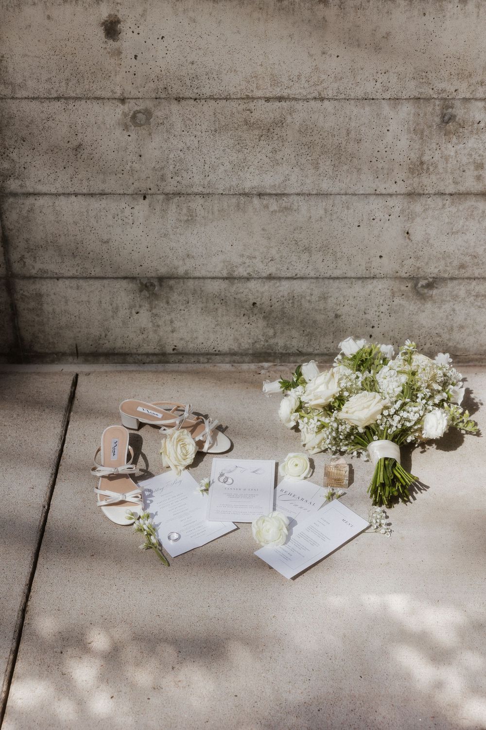 Wedding details with white floral bouquet and paper items arranged on concrete surface.