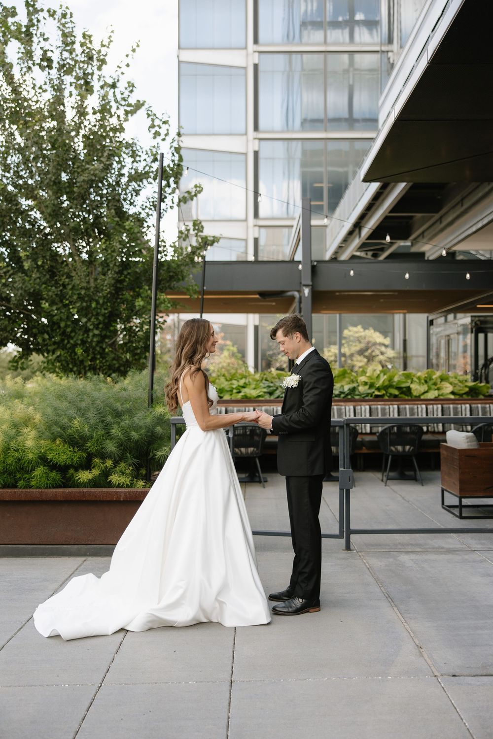 Wedding couple on modern terrace with glass building and greenery.
