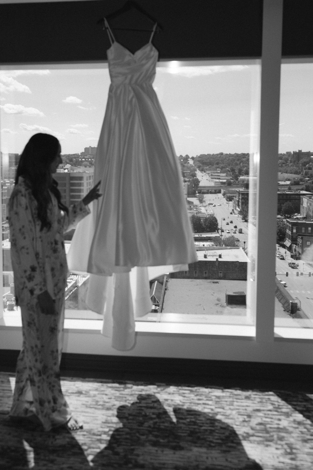 Wedding dresses hanging in a bright room with large windows overlooking a cityscape.