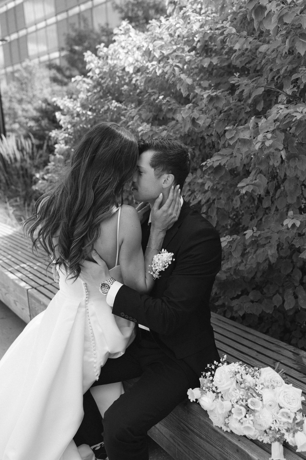 Romantic moment captured on outdoor bench surrounded by lush greenery.