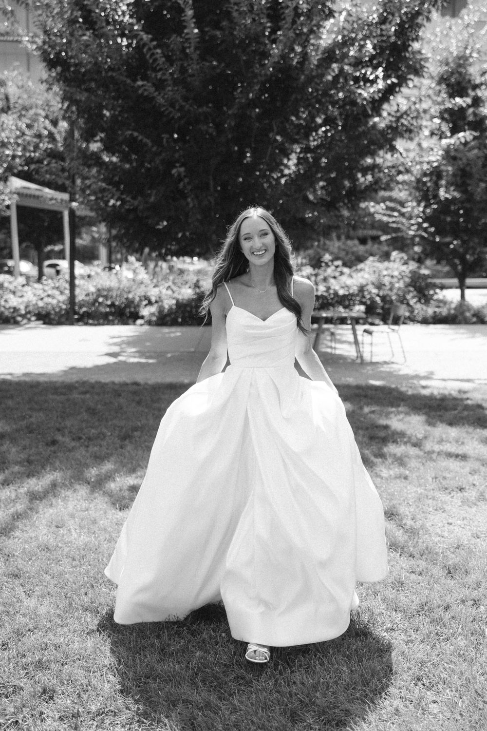 A flowing white wedding dress billows across a sunny grass lawn.