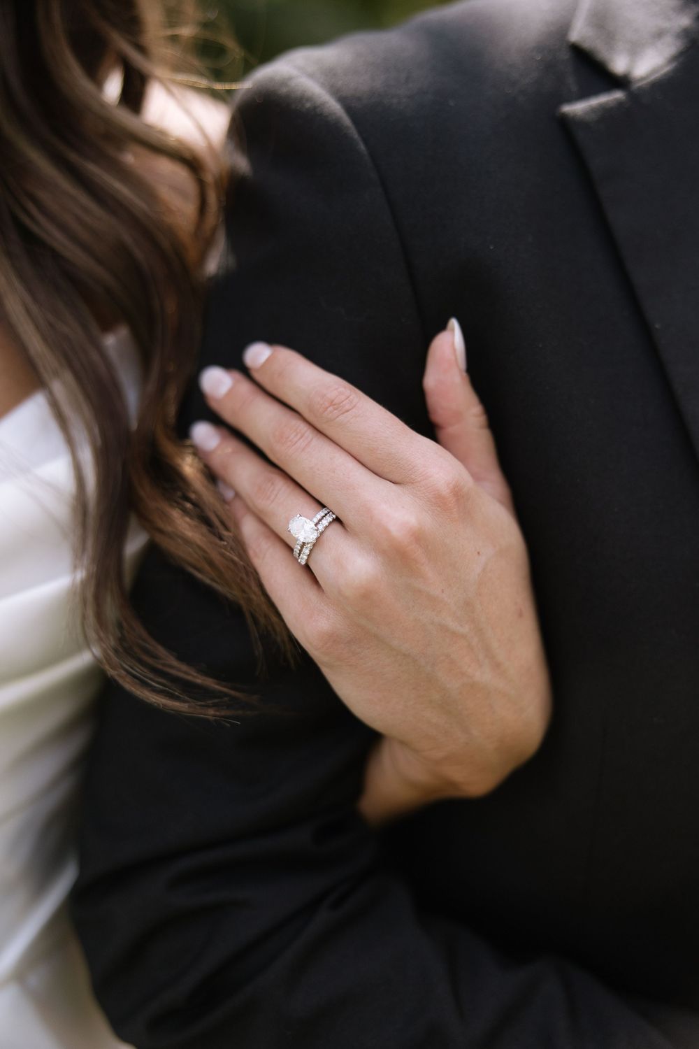 Close-up detail of hands wearing wedding rings against formal black and white attire.