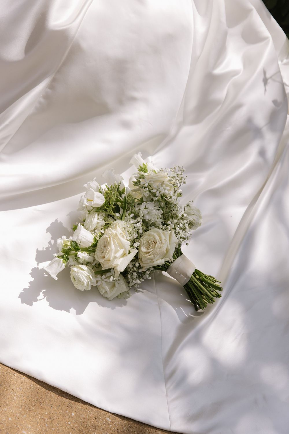 White roses and greenery bouquet arranged on flowing white satin fabric.