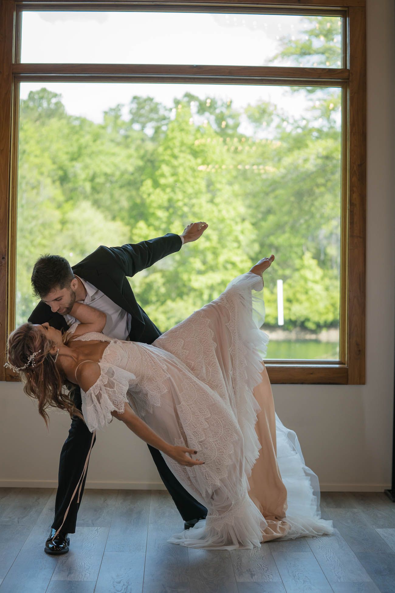 A couple performs a romantic dip dance move in a sunlit room with wooden floors and windows in Charleston, SC