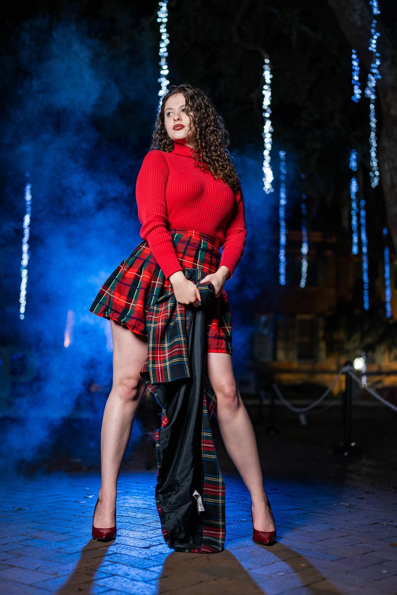 Fashion model in red sweater and plaid skirt poses dramatically with blue backdrop with smoke at Cistern in Downtown, Charleston, SC.