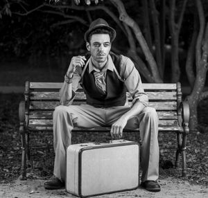 Black and white portrait of person sitting on bench with vintage suitcase at Hampton Park, Charleston, SC.